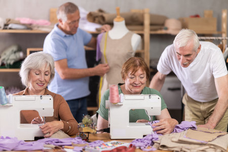 Senior man work with mannequin at sewing school studio, others people sew and talking