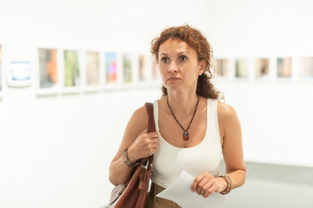 Middle-aged woman looking at pictures on wall in museum