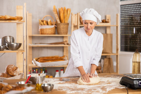 Middle-aged woman baker kneads the dough in bakery