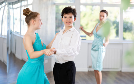 Couple of teenage dancers rehearsing ballroom dance with female teacher
