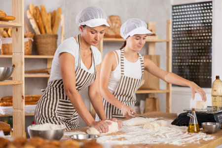 Girl helps an experienced baker prepare dough in kitchen of bakery - together they knead dough, cut...