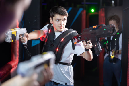 Emotional man with laser pistol playing laser tag with friends on dark labyrinthの写真素材