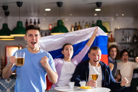 Group of excited young adult friends waving flag of Russia and supporting national team with beer in barの写真素材