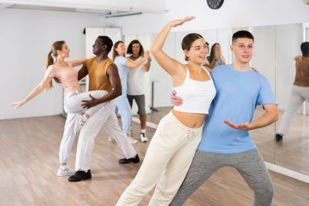 Smiling young adult couples dancing together in pairs and practicing new movements in modern studio