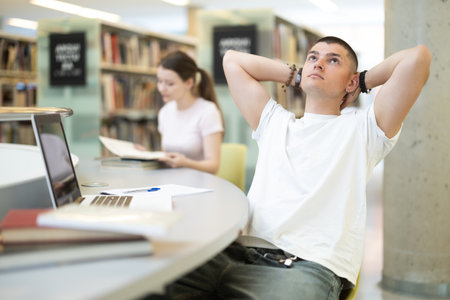 Tired guy student at a table in the libraryの写真素材