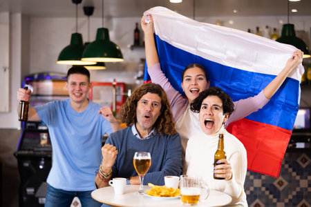 Happy friends of different ages drinking beer and celebrating the victory of the Russian team in night barの写真素材