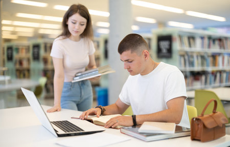 Female student asks male student working on laptopの写真素材