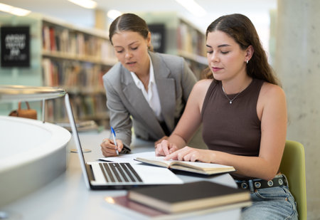 female student works at a notebook, and a fellow student helps herの写真素材
