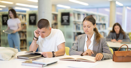Girl and guy are sitting at table in library - reading books, preparing for exams at university