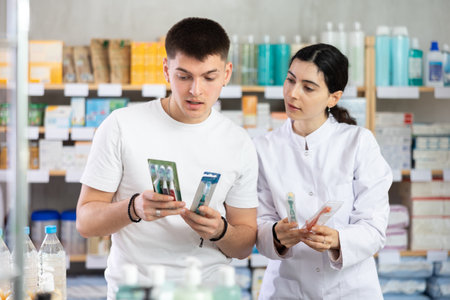Man chooses toothbrush in modern pharmacy. Female pharmacist helps with choosingの写真素材