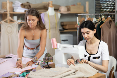 Female dressmaker sewing at machine while teammate pinning patterns to fabricの写真素材