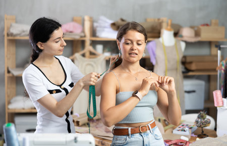 Female fashion designer taking body measurements of woman in tailoring studioの写真素材