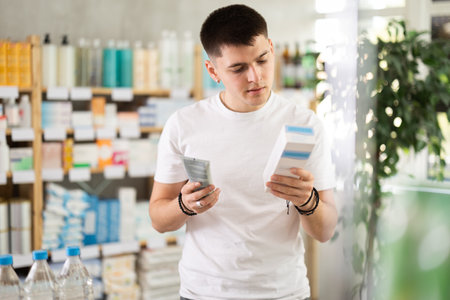 Young man choosing creams in pharmacyの写真素材