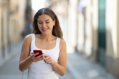 Happy woman looking to phone in hands and chatting in cityの写真素材