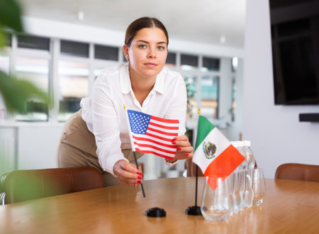 A woman in a white blouse with friendly smile arrangs flags of Mexico and The United States for meeting.の写真素材