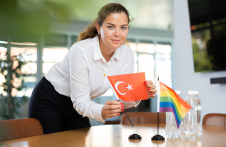 Young woman putting Turkish and LGBT flags on desk in officeの写真素材