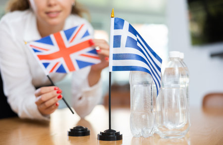 Unrecognizable girl sets midget flags of Greece and Great Britain before international negotiationsの写真素材
