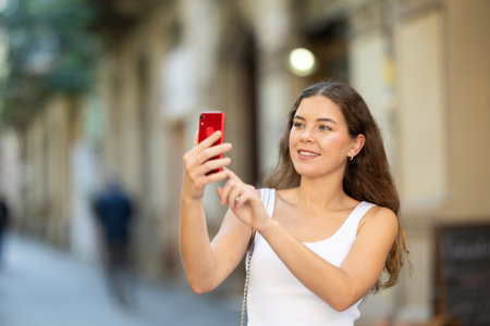 Young girl with mobile phone in her hands walking around the city and taking pictures of sightsの写真素材