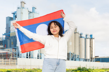 Happy asian girl with flag of laos standing in front of industrial sceneryの写真素材