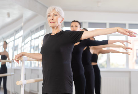 Girls in ballet class perform second position with participation of mature female mentor