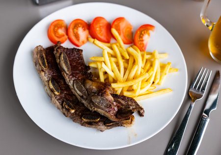 Spanish cuisine. Grilled beef ribs with a side dish of fresh tomatoes and fried potatoes