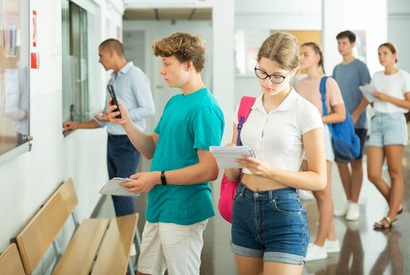 Teenage students checking exam schedule on bulletin board in collegeの写真素材