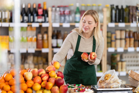 Female seller lays out ripe apples on store counter for saleの写真素材