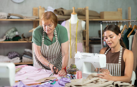 Mature woman cutting fabric next to female seamstressの写真素材