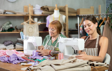 Elderly and young women seamstresses sewing on machineの写真素材