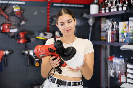Woman chooses and buys paint spray gun in hardware store