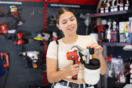 Woman choose examine handheld portable spray gun, airbrush in tools department of construction store