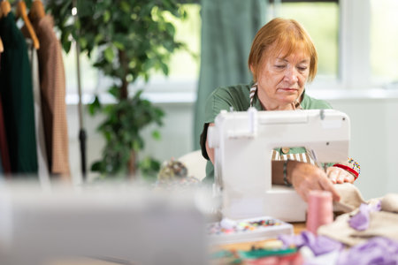 Woman seamstress sews on sewing machine in workshopの写真素材