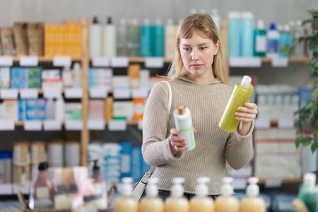 Female shopper in autumn clothes chooses medicated shampoo at pharmacyの写真素材