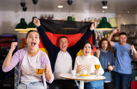 Company of screaming young adult sports fans waving flag of Germany and supporting national team...