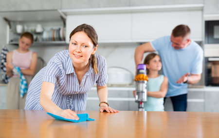 Mom is dusting the table. Father with children vacuuming roomの写真素材