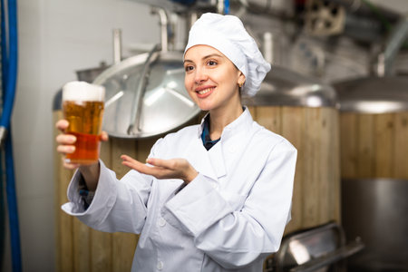 Portrait of positive woman brewmaster with glass of beerの写真素材