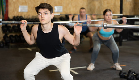 Motivated CrossFit male athlete lifting heavy body bar or barbell during group training in gym....