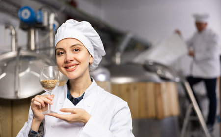 Portrait of positive female brewer with a glass of barley at brewery