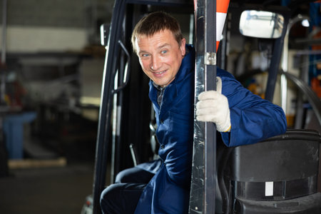 Positive middle-aged worker driving forklift in industrial workshop