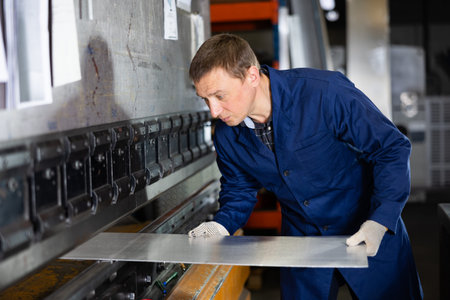 Metallurgical plant - male worker bending sheet of metal on press