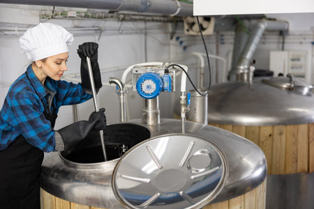 Focused female brewer mixing raw materials in fermenter