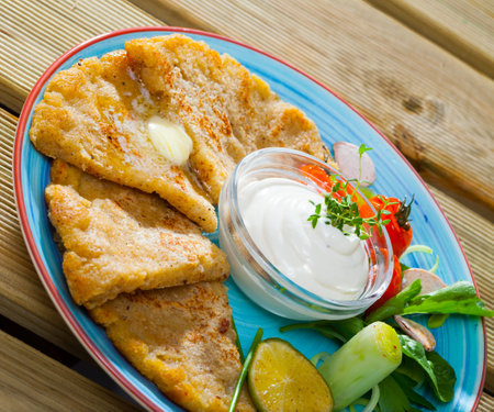 Potato pancakes with white sauce and vegetables on a blue plate.の写真素材
