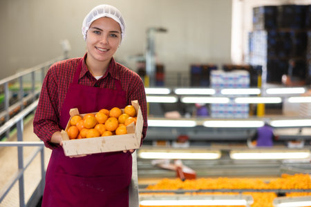 Glad positive female employee in colored uniforms hold a box of fresh ripe tangerines in their hands...