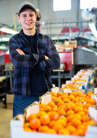 Smiling citrus sorting factory worker standing near boxes of tangerinesの写真素材
