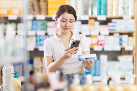 Female customer scanning QR code on box of ointment in pharmacyの写真素材