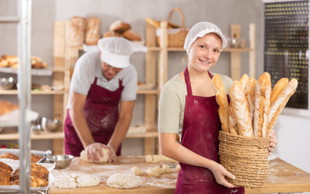 Smiling girl presenting freshly baked baguettes in family bakery