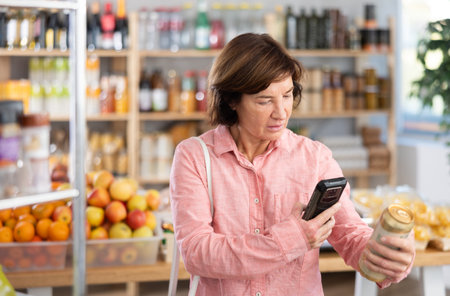 Mature woman is scanning QR on a can of beer in groceryの写真素材