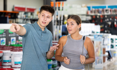 Young positive woman and man shopping in building store, man pointing to somethingの写真素材