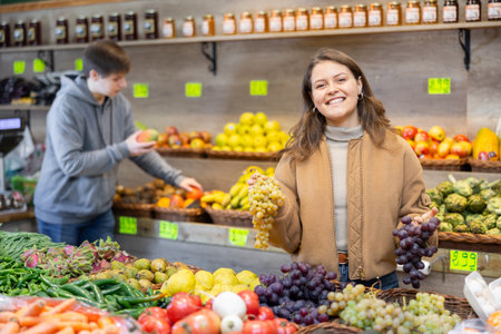 Girl purchaser choosing grape at the counter in grocery storeの写真素材