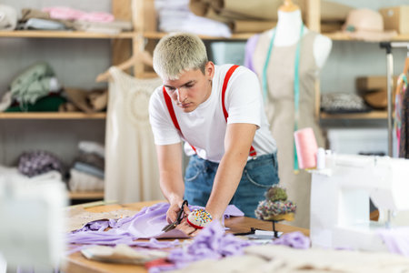 Attentive young tailor cutting textile in sewing studio